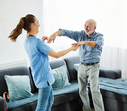 Doctor or nurse caregiver dancing and having  fun with senior man at home or nursing home
