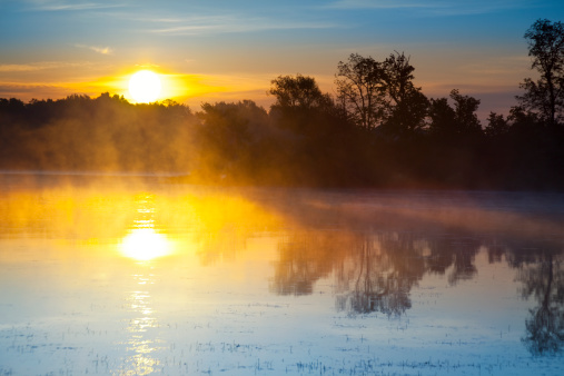 Mist comes off a pond on a golf course during a fiery sunrise