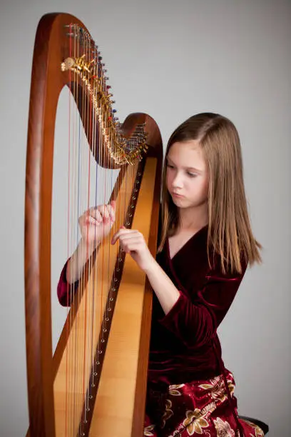 Serious 12-year old girl playing a harp on grey background.  