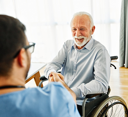 Portrait of senior elderly man with a doctor or male caregiver shaking hands at home or nursing home