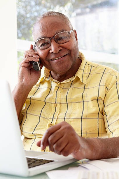 starszy człowiek na telefon za pomocą laptopa w domu - senior adult computer men mature adult zdjęcia i obrazy z banku zdjęć