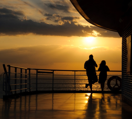 A silhouetted man and woman watching the sunset at sea. The skyline on the horizon is Miami - Ft. Lauderdale.