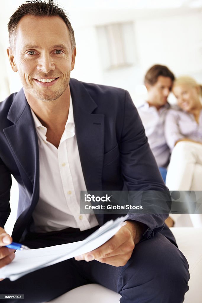 I'm a consultant that you can rely on! A handsome male consultant sitting with a couple in the background Business Stock Photo