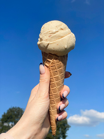 Stock photo showing close-up view of unrecognisable female, with black tipped nail art, holding a waffle cone with a scoop of toffee ice cream gelato whilst walking in Venice.