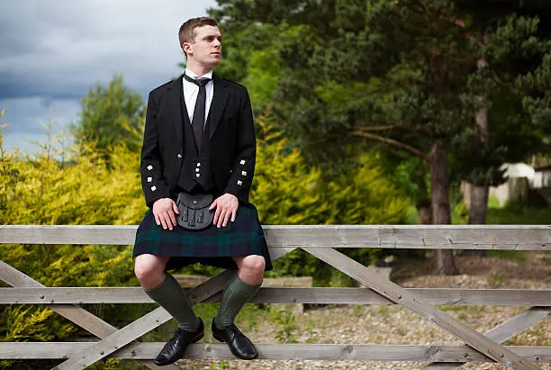 young scotsman sits on a wooden gate