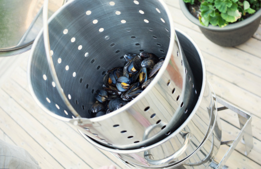 A large steamer of cooked mussels is lifted out for dinner.