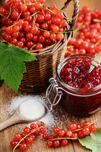basket with red currant on table and spoon filled with sugar as well as a currant jam glass jar.