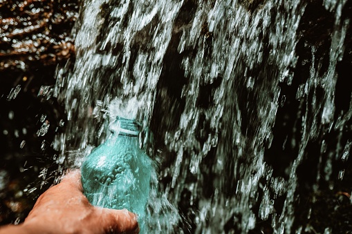 The flow of water from the waterfall fills the bottle