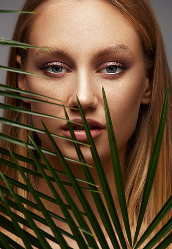 Blonde young beauty looking at the camera through green palm fronds.