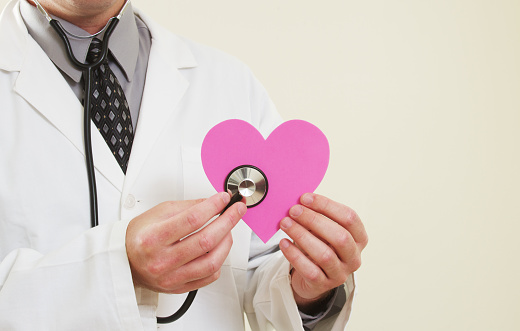 a male medical doctor checking the pulse of a pink heart shape. 