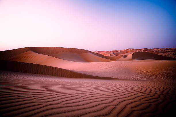 Large sand dunes in the desert reaching till the horizon at mystic twilight at night time, right after sunset / dusk.
