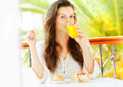 Portrait of an young attractive woman having fresh fruit breakfast and drinking fresh orange juice at balcony, outdoor