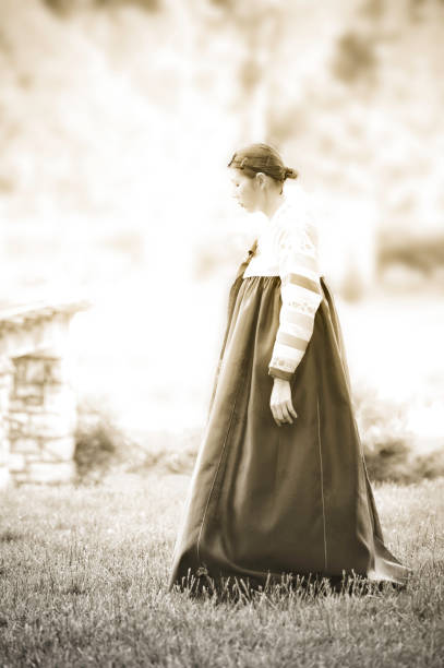 Young woman in medieval dress and cloak standing by tree in forest. Middle Ages.