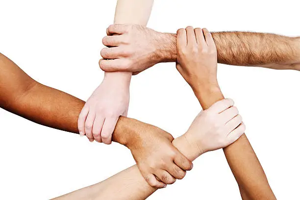 Five multiracial hands are joined together in unity, forming a linked pentagon shape, isolated against a white background. 