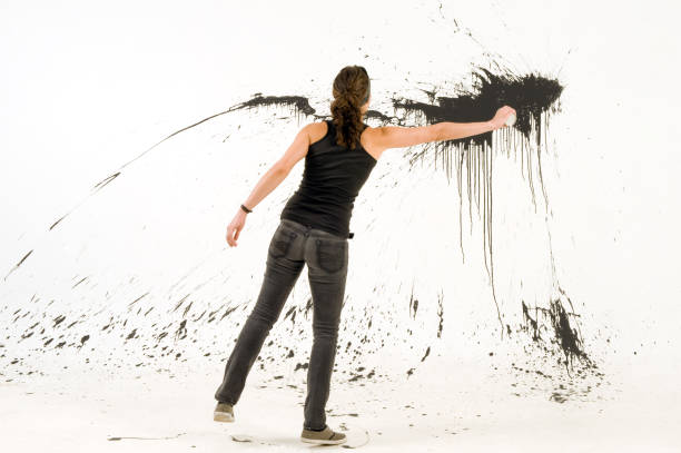 Artist draws on transparent glass surface. Person using large brush with acrylic oil medium white paint and drawing stroke directly on black glass screen isolated background, opposite view scene.