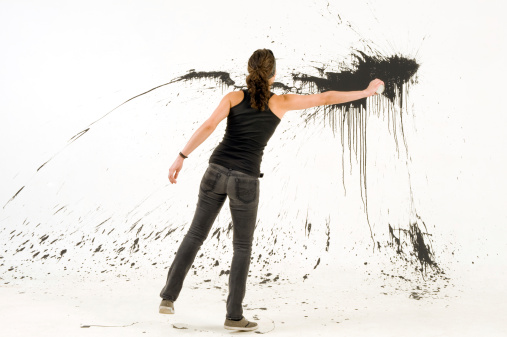 woman artist splashing the white wall with black paint.