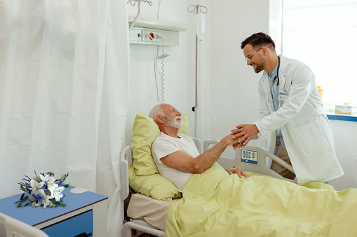 Hospital Ward: Male Doctor Talking to Senior Male Patient in Hospital Bed