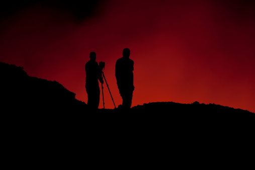 Two scientists standing on the crater rim of Erta Ale - one of the most active vulancoes in the world with an active, red glowing lava lake. 