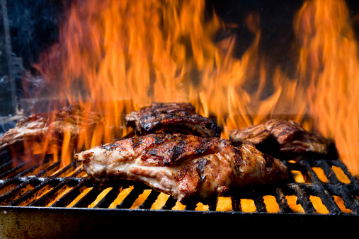 Baby Back Ribs on a Flaming old fashioned barbecue grill with fire surrounding the meat.  All the meat has perfect grill marks and is ready to come off the heat and be eaten
