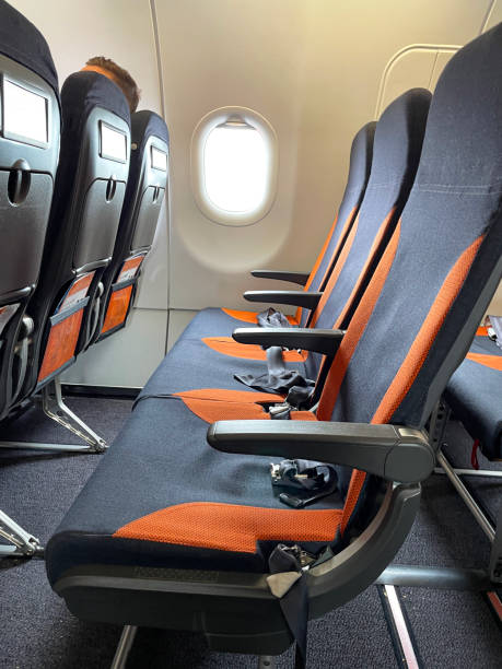 istock Close-up image of airplane cabin interior, foldable table in seat back, rows of empty seats with safety belts lying on cushion, focus on foreground 1685186955
