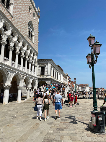 Venice, Italy - July 12, 2023: Stock photo showing close-up view of tourists and locals walking along the Riva degli Schiavoni past the Doge's Palace (Palazzo Ducale) towards Ponte della Paglia (Straw bridge) spanning the Rio di Palazzo waterway, Venice, Italy.