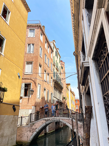Venice, Italy - July, 12 2023: Stock photo showing close-up view of tourists standing on one of the many bridges crossing the narrow canals lined with old buildings in Venice, Italy.