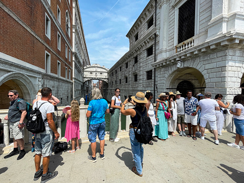 Venice, Italy - July 12, 2023: Stock photo showing close-up view of group of tourists gathered on Ponte della Paglia (Straw bridge) over the Rio di Palazzo to take photographs of the Ponte dei Sospiri (Bridge of Sighs) in the background.