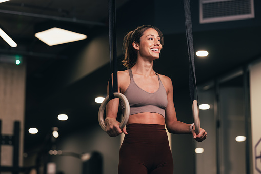 A smiling Caucasian athlete holding gymnastics rings while doing her training in the gym.