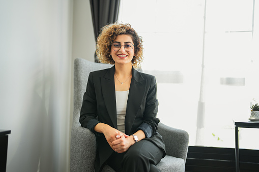 Smiling businesswoman in black jacket with curly hair sitting on sofa in office