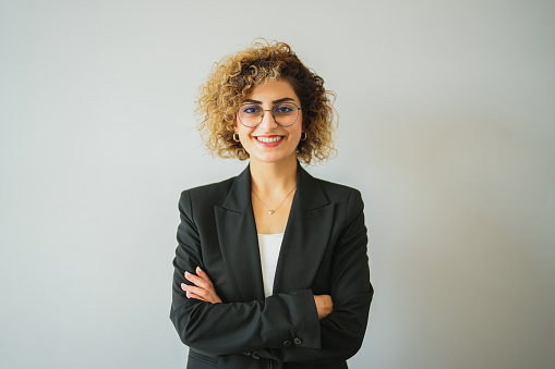 Businesswoman with curly hair in black jacket with arms crossed in front of white background in the office