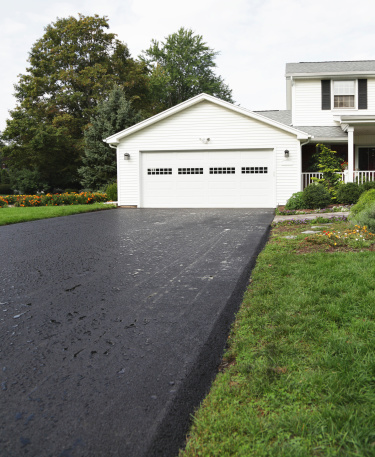 Photo shot the day after a brand new residential home blacktop asphalt driveway was completed - with overnight rain puddles beading on the still oily surface. This is an 