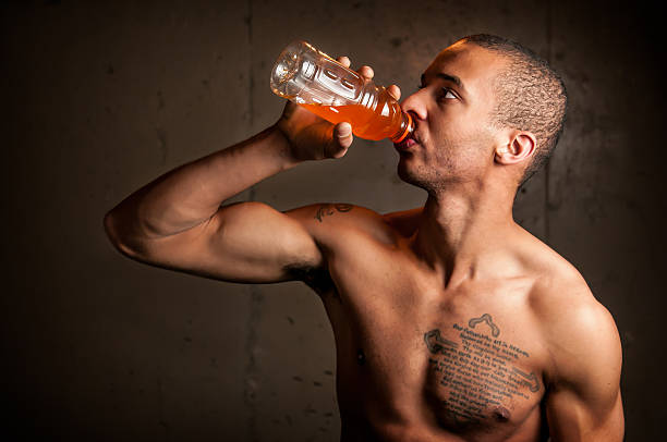 Young adult black male drinking a sports drink in a dark grungy setting.  Some copy space on the left.