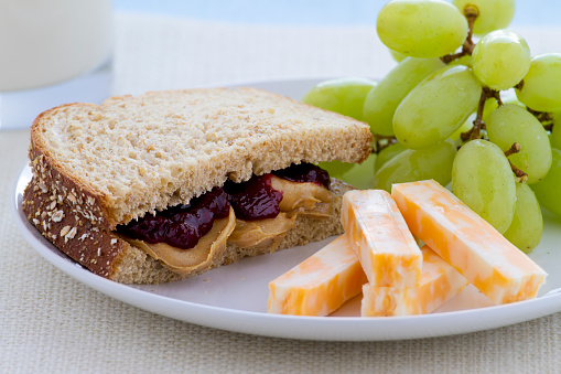 Peanut butter jelly sandwich on wheat bread with green grapes and cheese.