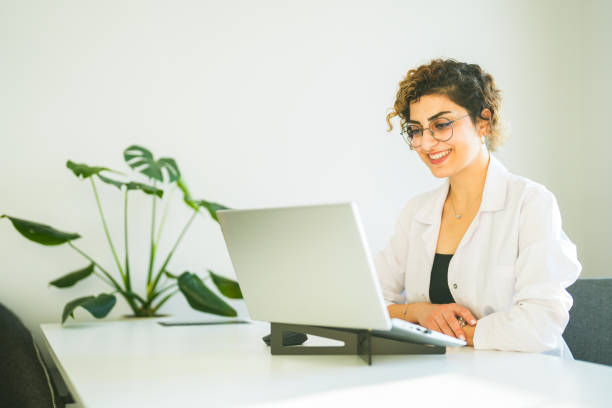 istock curly haired woman in white uniform working from laptop in office 1685314098