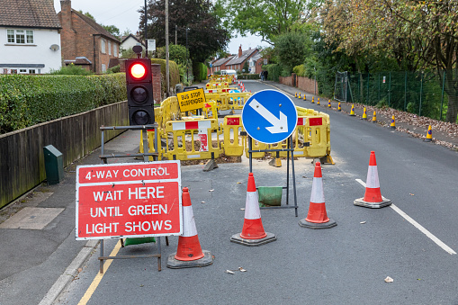 UK roadworks digging up local road tarmac to repair utility pipework underground with safety barriers and signs