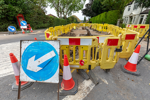 UK roadworks digging up local road tarmac to repair utility pipework underground with safety barriers and signs
