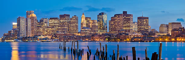 Boston Cityscape in Early Evening - Panorama View of Boston looking across Boston Harbor from East Boston. As night begins to fall, the lights of Boston's numerous skyscrapers glow on the calm waters of Boston Harbor. east boston stock pictures, royalty-free photos & images