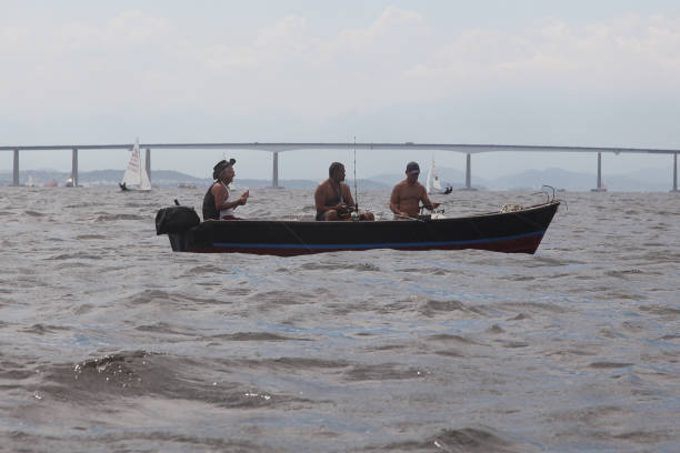 Rio de Janeiro, Brazil – September 10, 2023: three Rio fishermen in a small boat fishing in Guanabara Bay. In the background you can see the Rio Niteroi bridge