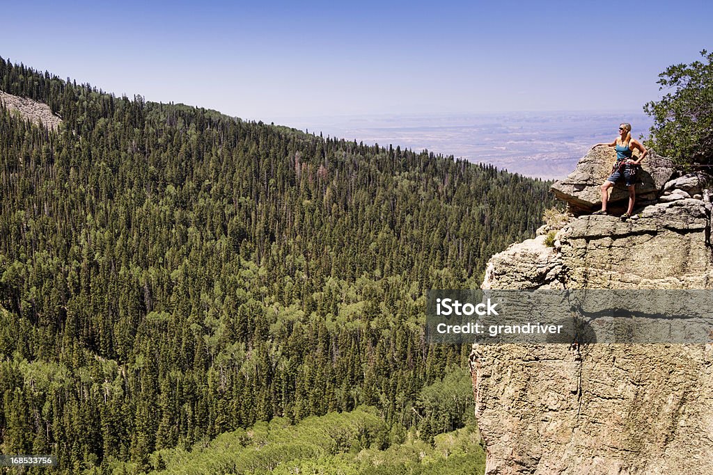 Female Mountain Climber Female Mountain Climber on a mountain cliff posing and looking out at the vista.  She has just climbed a sheer granite face and is looking at a beautiful green pine forest in the distance. Colorado Stock Photo