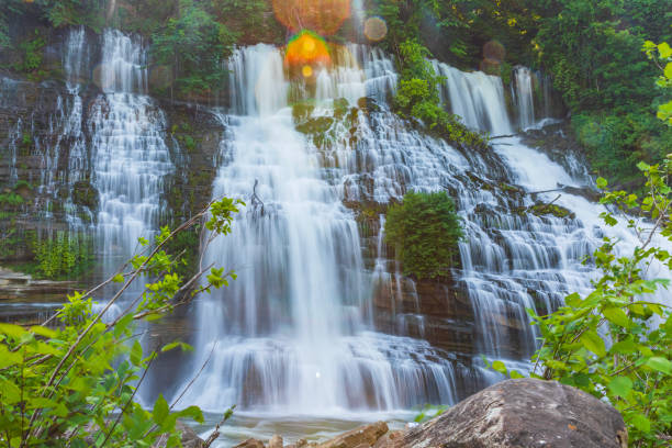 Large waterfall flowing over rocks into river framed by lush golden foliage in soft warm light
