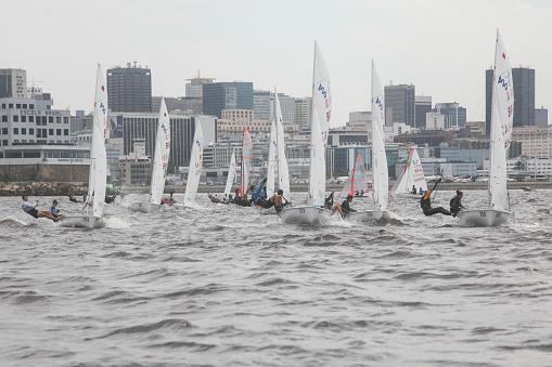 Rio de Janeiro, Brazil – September 10, 2023: several sailors in the 420 class sailboat regatta on a very windy and rainy day in Guanabara Bay during the Rio de Janeiro sailing week. In the background the city of Rio de Janeiro financial district.