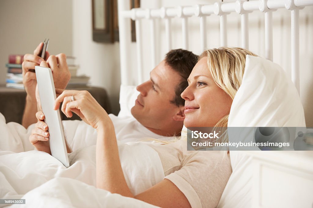 Par usando tableta Digital y teléfono móvil en la cama - Foto de stock de 20 a 29 años libre de derechos