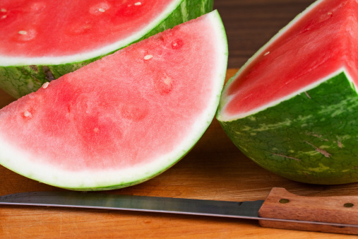 Sliced hybrid seedless watermelon with knife on a wood cutting board.