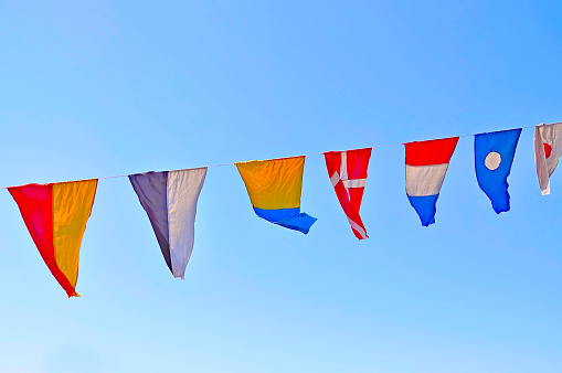 Flags of different countries on a rope against a blue sky.