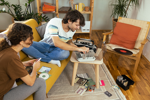 Couple enjoying at home, checking their old cd's and audio cassettes and enjoying music from the retro cd player