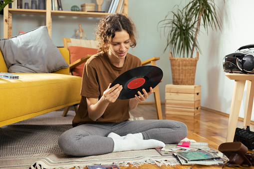 Young woman sitting at home, checking her old records and audio cassettes and enjoying music