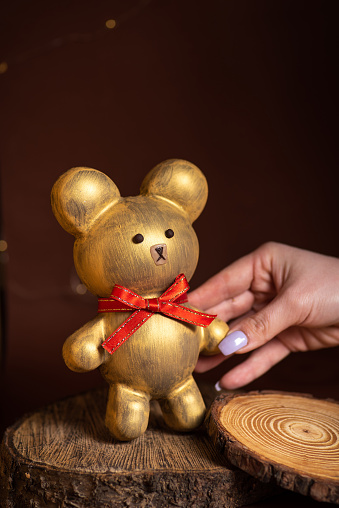 Woman's hand holding an edible figure of a bear in golden color. With a red bow. Unique and charming gift