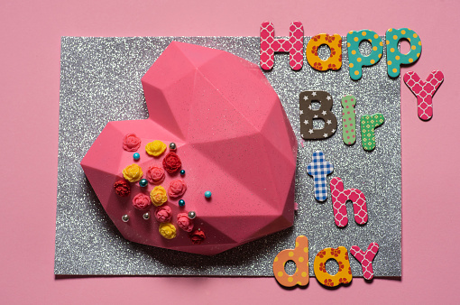 Pink heart-shaped cookie. Decorated with colorful small roses and sprinkled with glitter. On a sparkling background. Cute birthday present