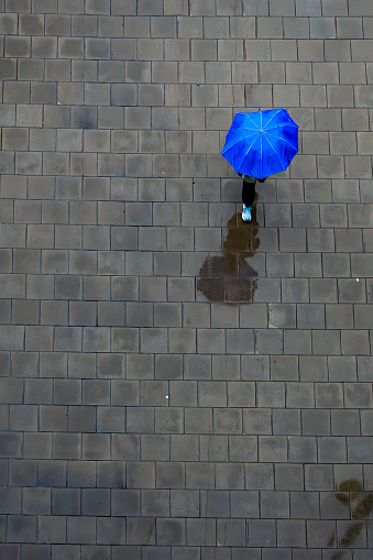 Stockholm, Sweden An unidentified person walks  on the sidewalk in the rain with a blue umbrella.