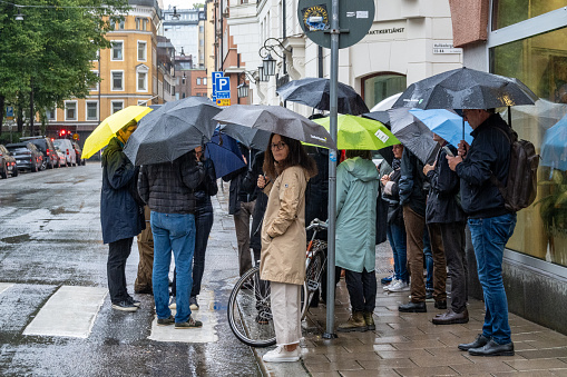 Stockholm, Sweden Sept. 1 2023 A group of people on a street corner downtown with umbrellas.